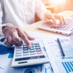 Bokföring - man vid dator som använder miniräknare