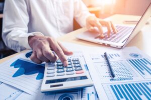 Bokföring - man vid dator som använder miniräknare