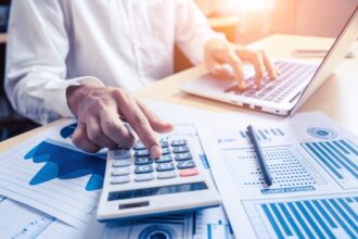 Bokföring - man vid dator som använder miniräknare